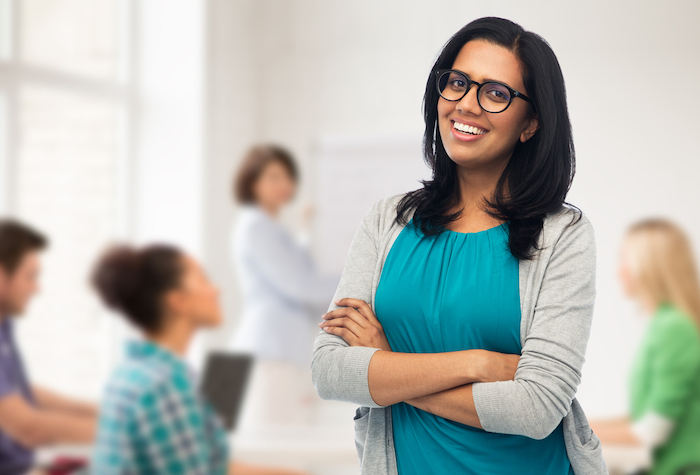 education, high school and people concept - happy smiling young indian woman or teacher in glasses over classroom background. happy for managed services.