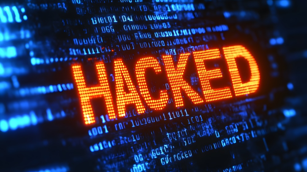 The image displays the word "HACKED" in bright orange over a digital display of code.